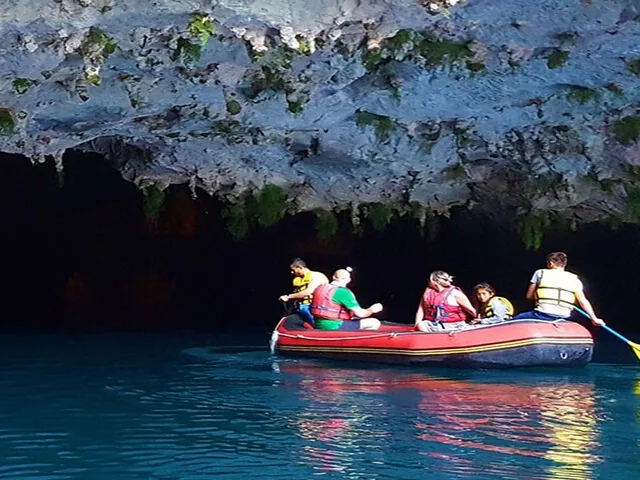 Menschen in einem roten Schlauchboot, die von leuchtend blauem Wasser in eine dunkle Höhle einfahren