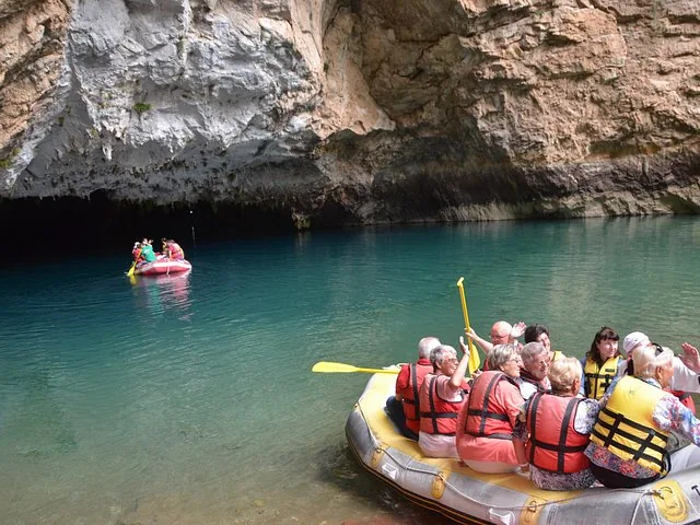 Group of people in a red raft exploring a cave with clear blue water