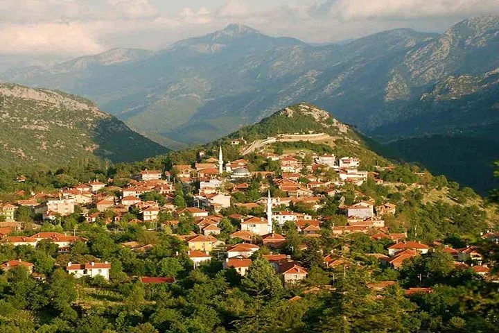 Malerischer Blick auf ein Dorf mit rotbedachten Häusern, eingebettet zwischen Hügeln und Bergen.