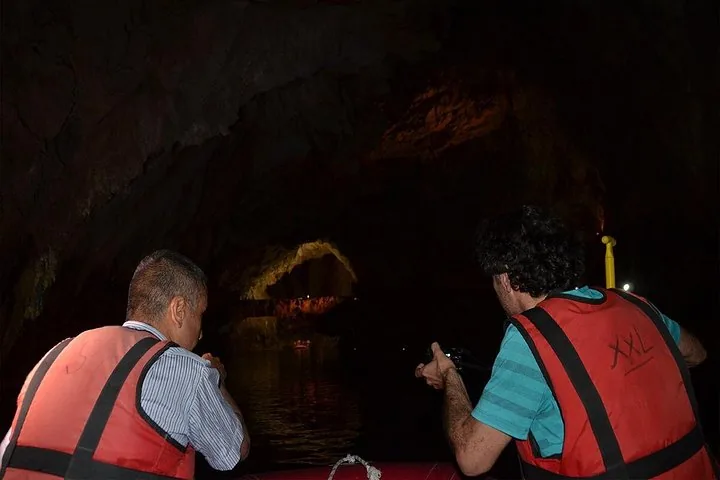 Zwei Personen in einem Schlauchboot in einer dunklen Höhle, eine hält eine Kamera