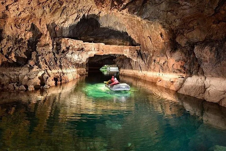 Deux personnes dans un radeau avançant dans un chenal d'eau claire à l'intérieur d'une grotte