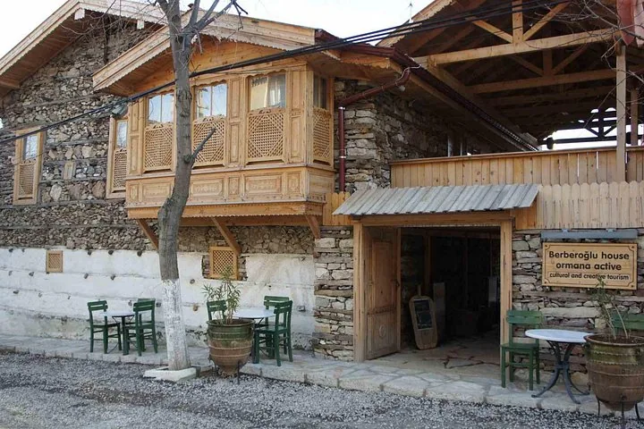 Exterior de un edificio tradicional de piedra y madera con el cartel de casa Berberoğlu y asientos al aire libre